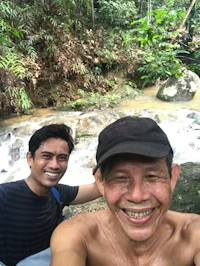 two men taking a selfie next to a waterfall