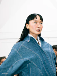 a woman in a blue denim jacket standing in front of a crowd