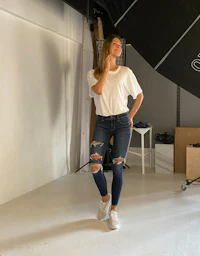 a woman in ripped jeans standing in front of a camera