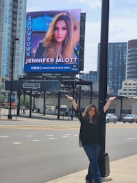 a woman standing in front of a billboard with her arms outstretched