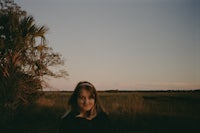 a woman standing in a field with palm trees