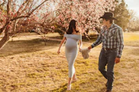 a man and woman walking through a park with blossoming trees