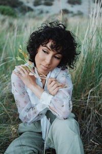 a woman with curly hair sitting in the grass