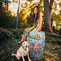 a girl sits on a wooden bench with an octopus painted on it