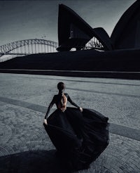 a woman in a black dress standing in front of the sydney opera house