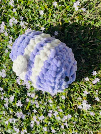 a purple and white stuffed animal laying in the grass