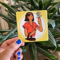 a hand holding a yellow sticker with a woman holding a bouquet of flowers