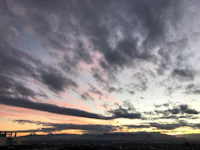 a sunset over a city with clouds and mountains in the background