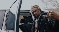a man with dreadlocks standing next to a car