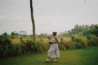 a woman in a white dress walking through a grassy field