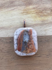 a square pendant with an orange stone on it