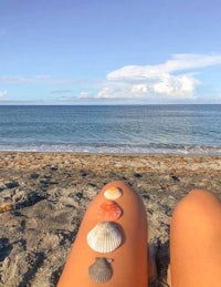 a woman sitting on the beach with seashells on her legs