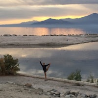 a woman standing in front of a body of water at sunset