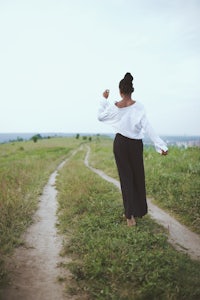 a woman walking down a dirt path in a field