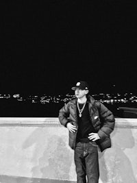 a black and white photo of a man leaning against a wall at night
