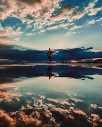 a person standing in a puddle with clouds reflected in it