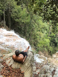 a man resting on a rock next to a waterfall