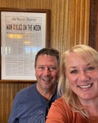 a man and a woman taking a selfie in front of a newspaper