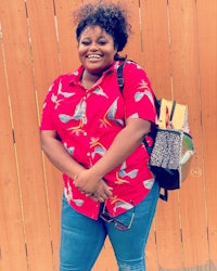 a woman wearing a red shirt and jeans is standing next to a fence