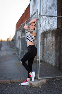 a woman in a checkered top leaning against a fence