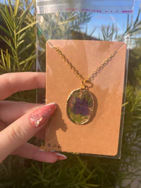 a hand holding a necklace with a purple flower on it