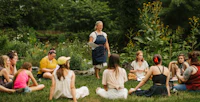a woman in an apron is talking to a group of people in a garden