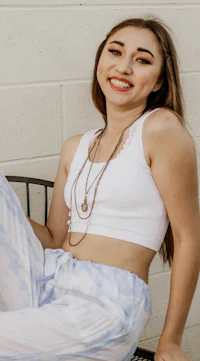 a young woman sitting on a bench wearing a white top and blue pants