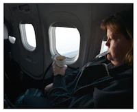 a woman sitting in an airplane holding a cup of coffee