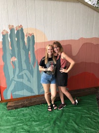 two women standing in front of a painted cactus