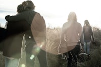 a group of people walking through a field with the sun behind them