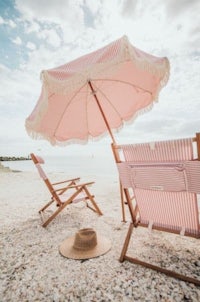 a pink striped umbrella and chairs on a beach