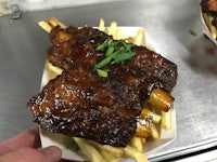 a person is holding ribs and fries in a container