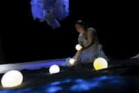 a woman in a white dress is playing with balls in the dark