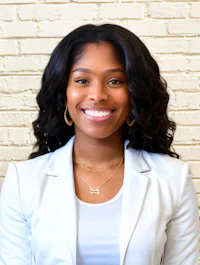 a woman in a white blazer smiles in front of a brick wall