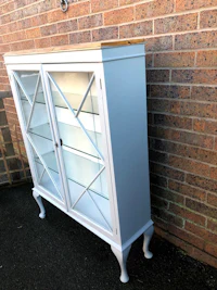 a white cabinet with glass doors and a brick wall