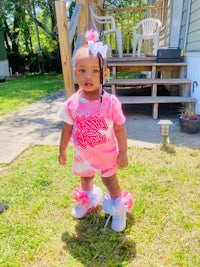 a baby girl wearing a pink t - shirt and pink sneakers