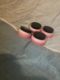 three pink jars sitting on top of a bed