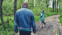 a man and woman walking down a dirt road in the woods