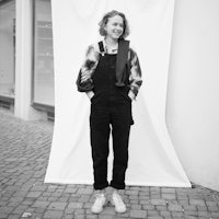 a woman in overalls standing in front of a brick wall