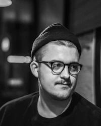 a black and white photo of a man wearing glasses and a beanie
