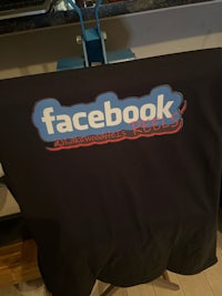 a black t - shirt with a facebook logo on it
