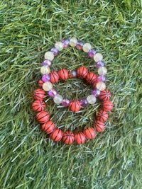 two bracelets with orange and red beads on the grass