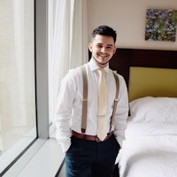 a man in a tie and suspenders standing in front of a bed