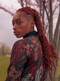 a woman with red dreadlocks standing in front of a tree