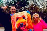 a man and woman posing with a painting of a dog