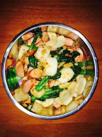 a bowl filled with potatoes and greens on a wooden table