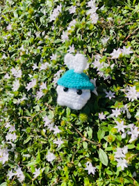 a crocheted hat with a blue hat sitting in a bush