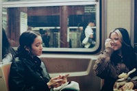 two women sitting on a train talking on their cell phones