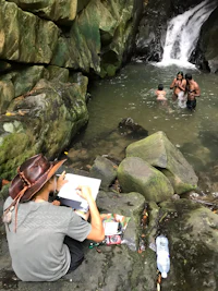 a man is drawing in the water near a waterfall