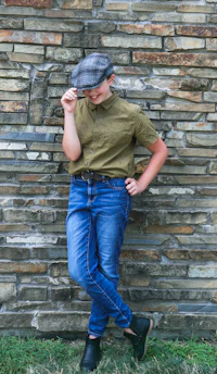 a boy in jeans and a hat leaning against a brick wall